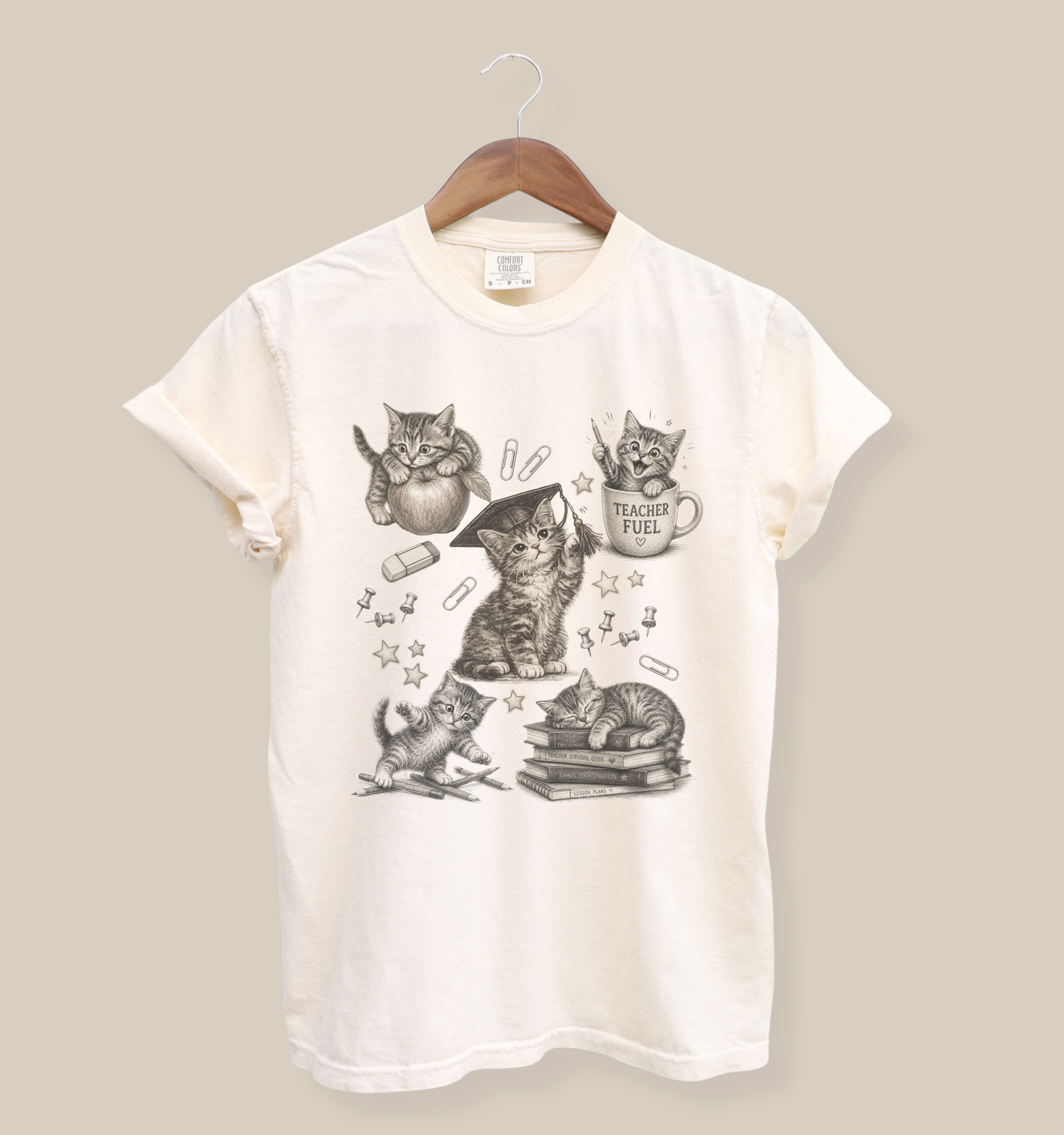 Comfort Colors 1717 t-shirt in ivory featuring vintage-style kitten illustrations with school-themed elements including books, pencils, paper clips, and a “Teacher Fuel” coffee mug.