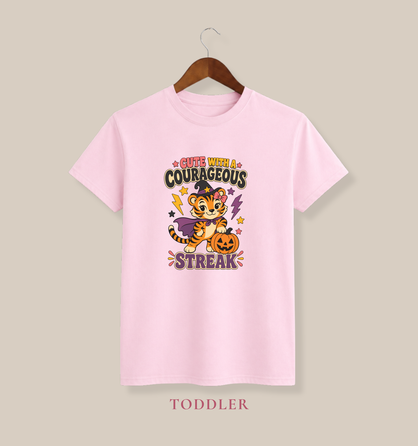 Pink toddler T-shirt featuring a tiger dressed as a witch, a jack-o’-lantern, colorful stars, and the phrase “Cute With a Courageous Streak.”