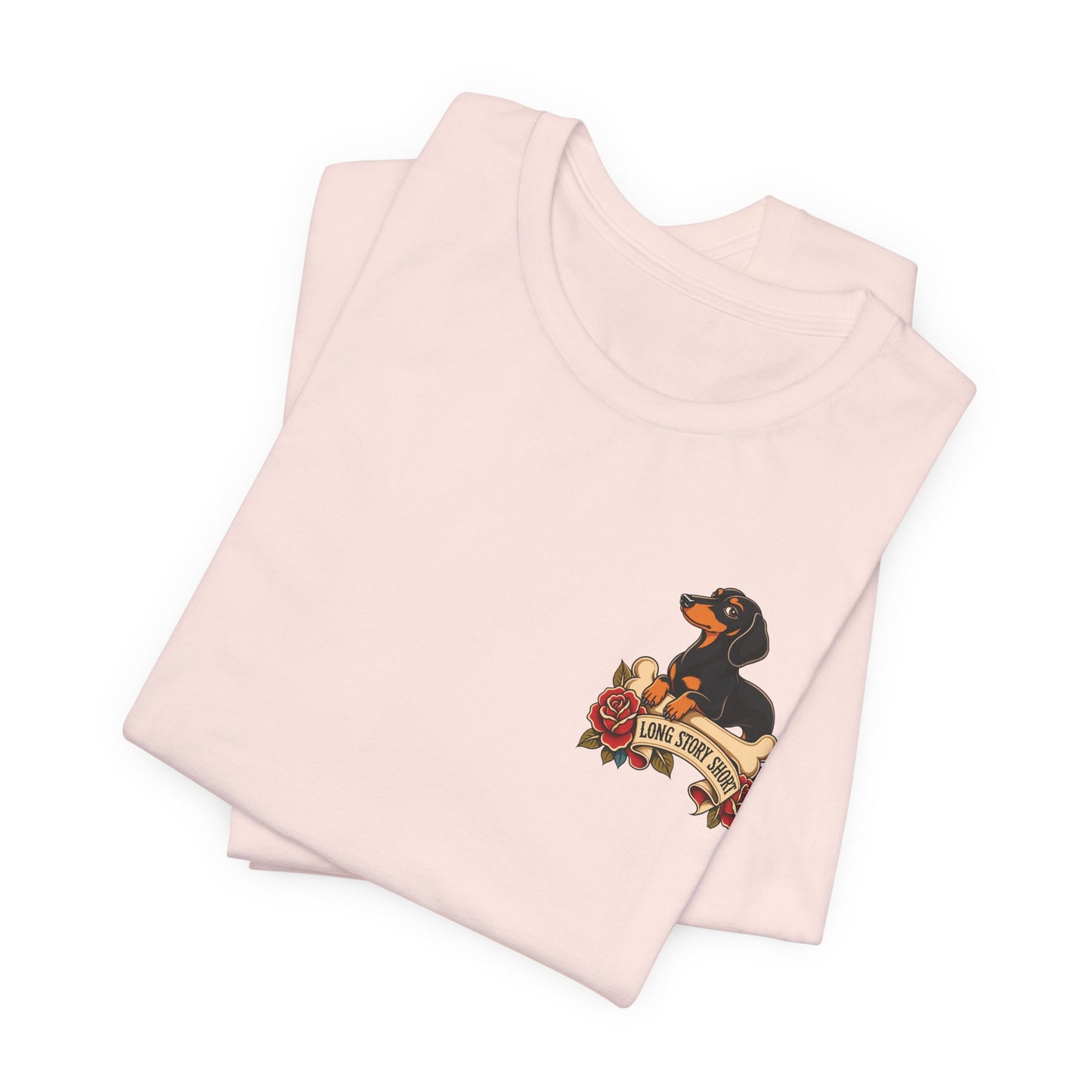 Soft pink adult T-shirt featuring a black and tan wiener dog perched above roses and the playful saying “Long Story Short.”