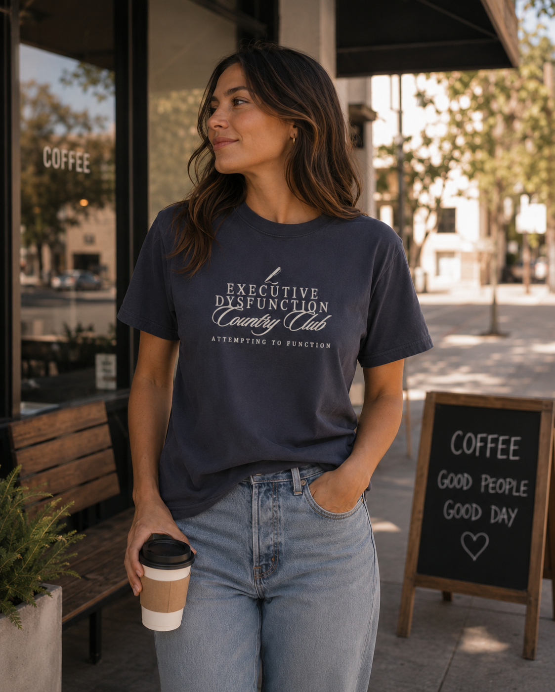 Woman wearing a navy Comfort Colors 1717 t-shirt featuring a cream “Executive Dysfunction Country Club” graphic with “Attempting to Function” text while holding coffee outside a café.