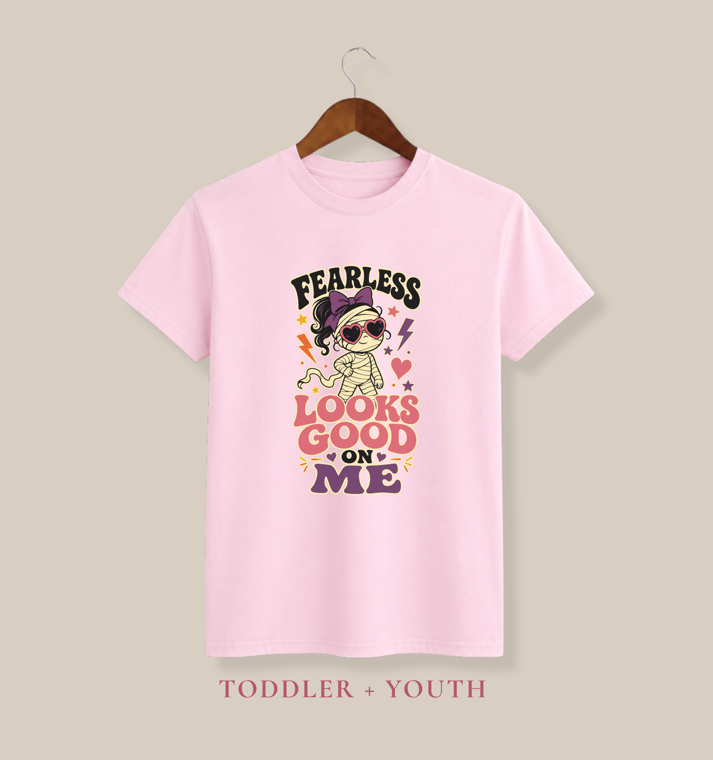 Pink youth T-shirt featuring a fashionable mummy in heart-shaped sunglasses, a purple bow, colorful stars, and the phrase “Fearless Looks Good on Me.”