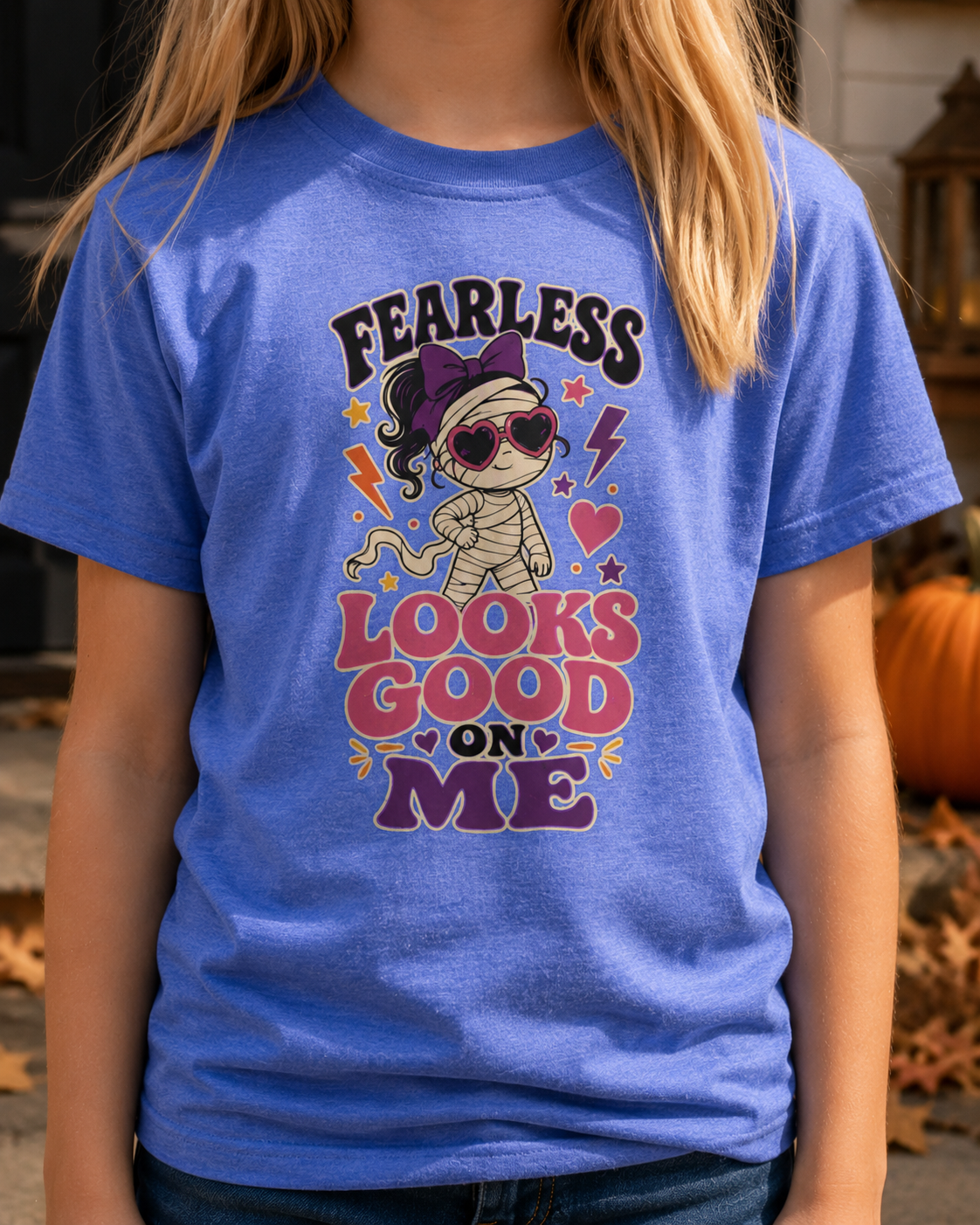 Girl wearing a heather Columbia blue youth T-shirt featuring a stylish mummy in heart-shaped sunglasses, colorful stars, lightning bolts, and the phrase “Fearless Looks Good on Me.”