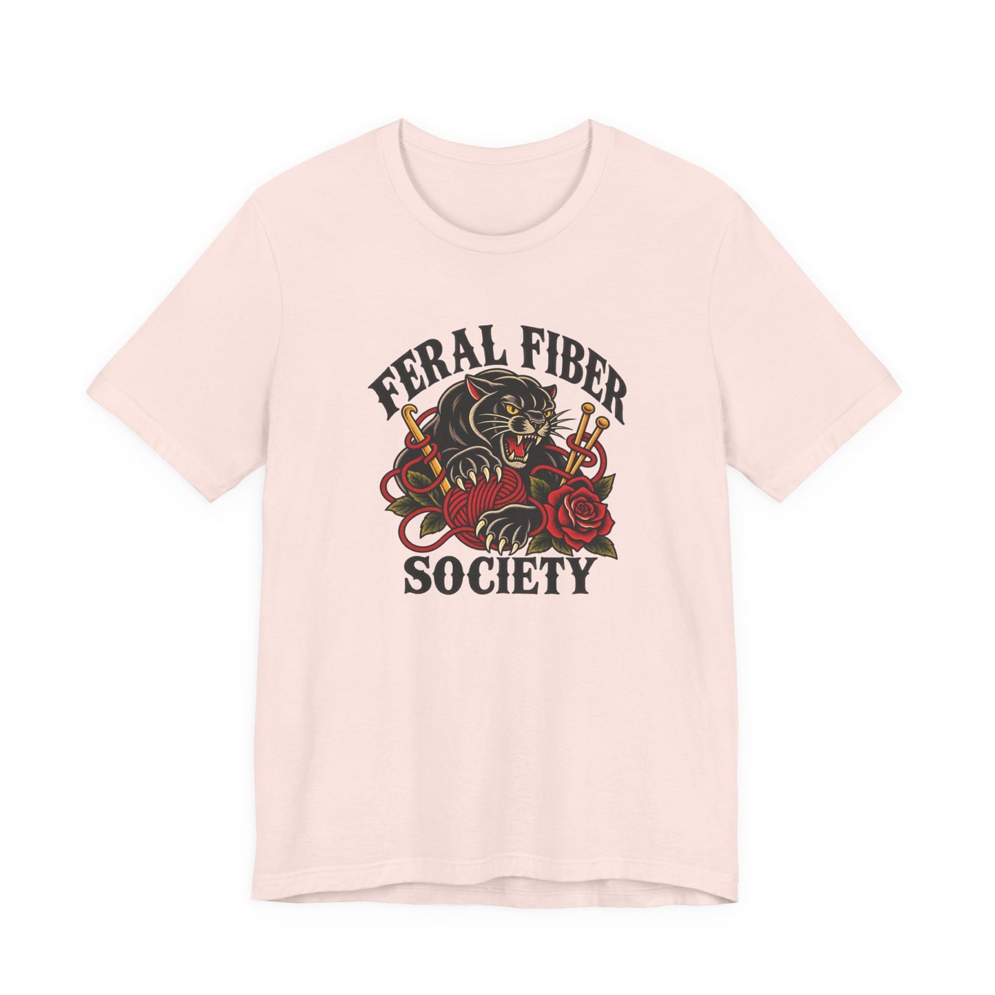 Soft pink classic fit tee displaying a retro Feral Fiber Society design with a black cat, red yarn ball, knitting needles, and floral accents.