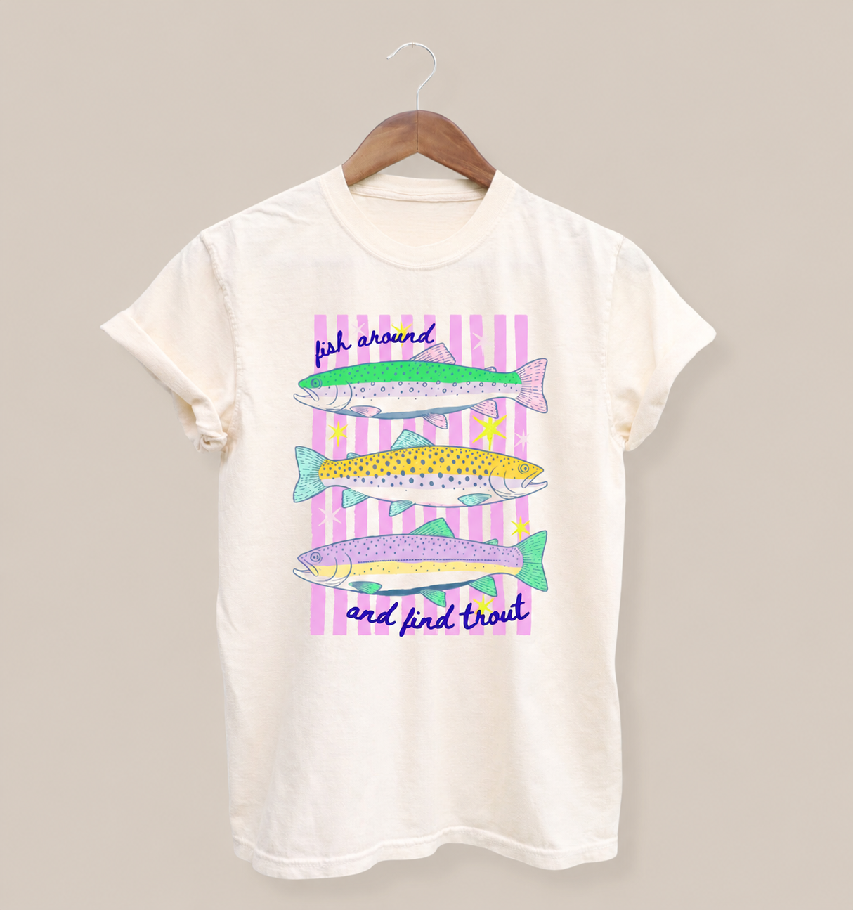 Ivory Comfort Colors 1717 t-shirt with a colorful fishing graphic featuring three illustrated trout, pink striped accents, and the phrase “Fish Around and Find Trout” on the front.