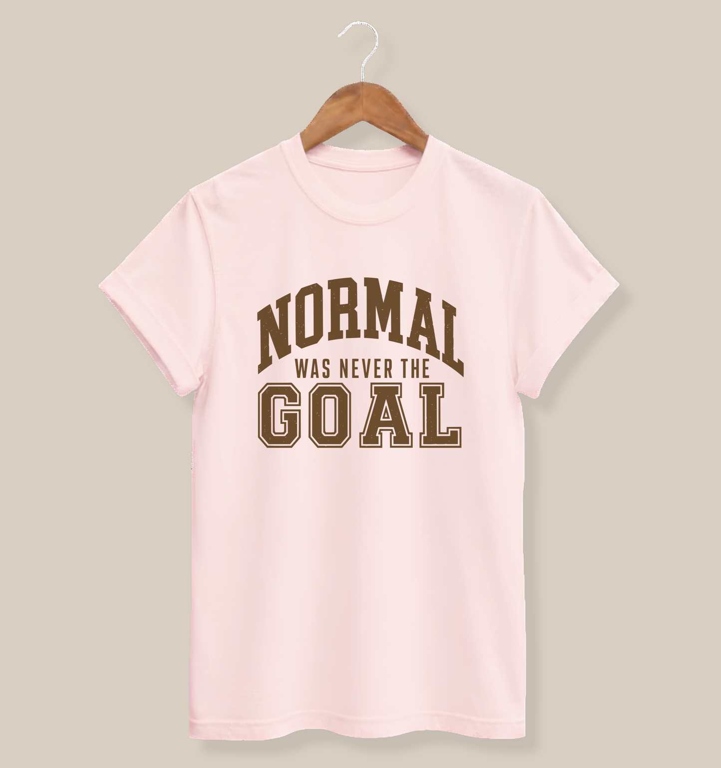 Soft pink adult T-shirt featuring bold collegiate-style typography with the playful saying “Normal Was Never the Goal.”