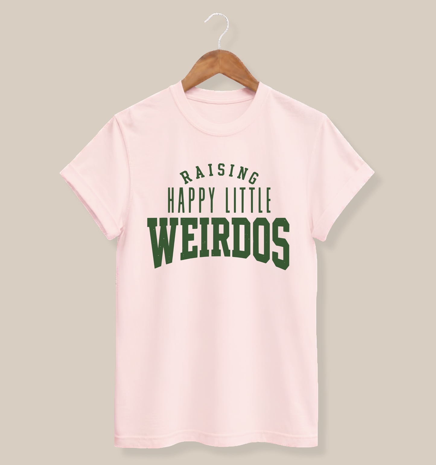 Soft pink adult T-shirt featuring bold collegiate-style typography with the humorous saying “Raising Happy Little Weirdos.”
