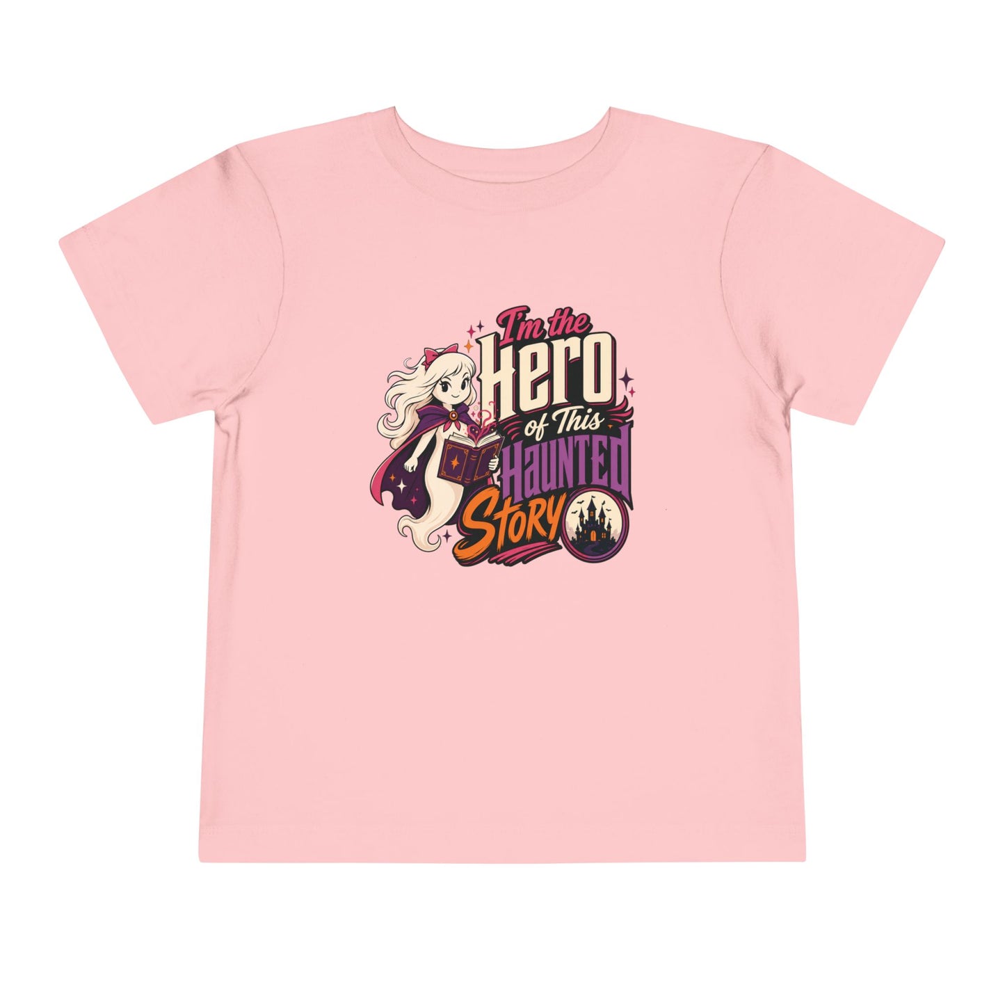 Pink toddler T-shirt featuring a caped ghost reading a spell book, a haunted castle, colorful stars, and the phrase “I’m the Hero of This Haunted Story.”