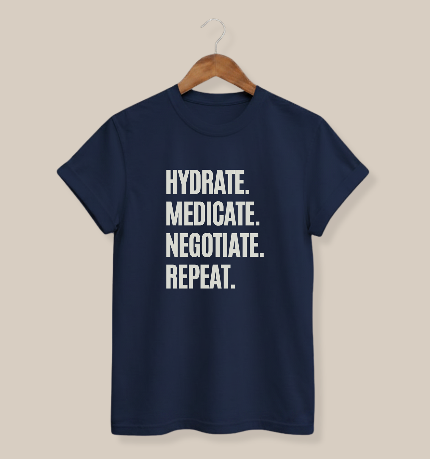 A navy blue short-sleeve t-shirt hanging on a wooden hanger against a solid beige background. The shirt features the text "Hydrate. Medicate. Negotiate. Repeat."