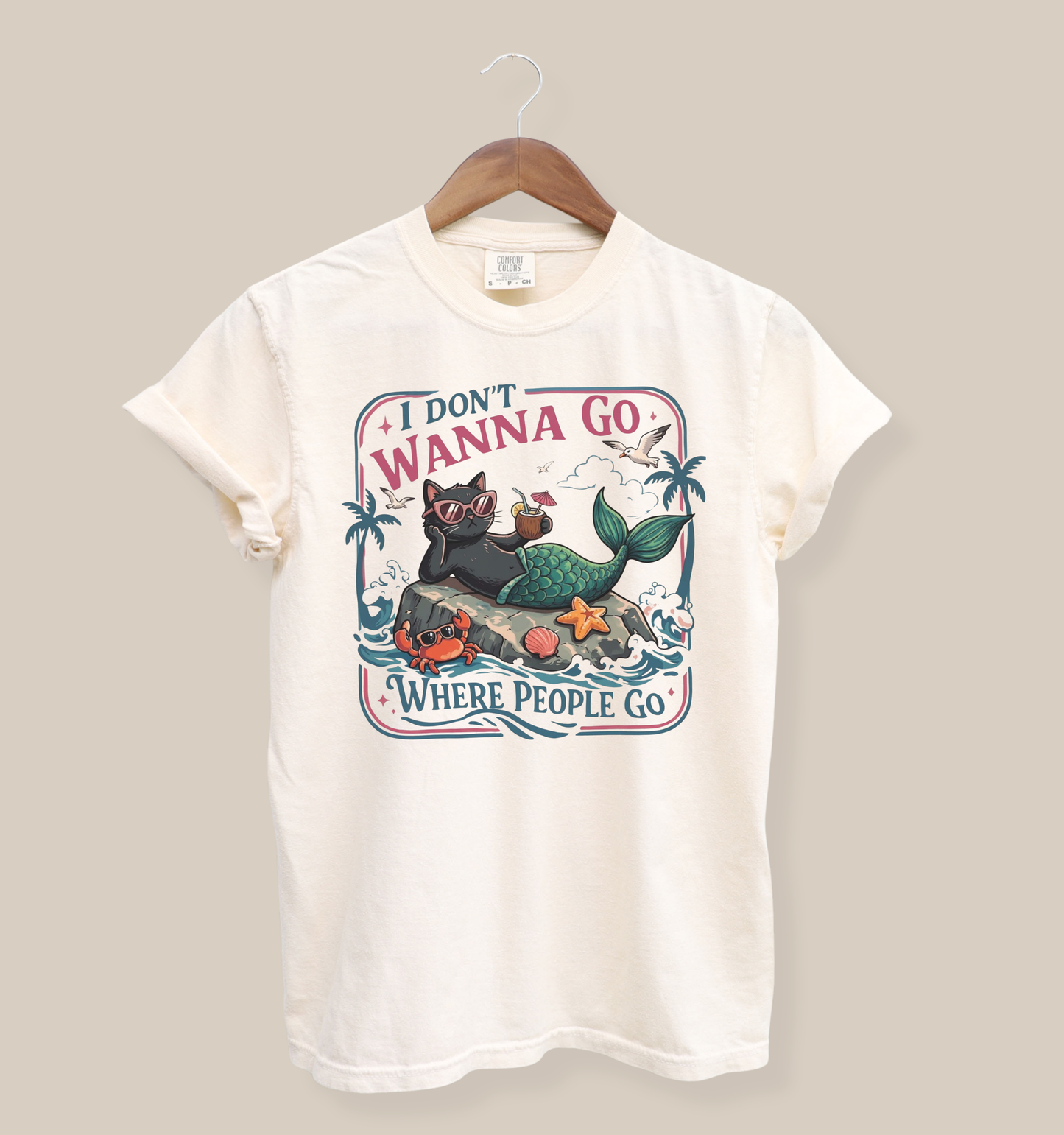 Bella + Canvas 3001 t-shirt in natural featuring a funny introvert-inspired graphic of a black cat mermaid wearing sunglasses, lounging on a rock with the phrase “I Don’t Wanna Go Where People Go” surrounded by beach and ocean artwork.