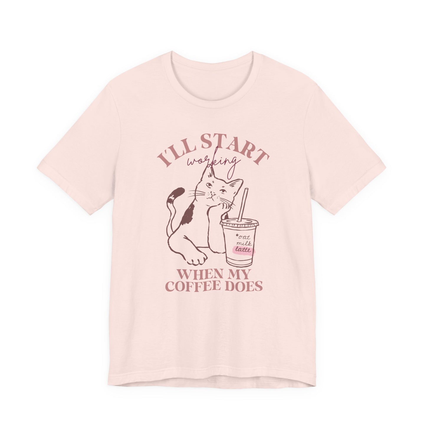 Bella + Canvas 3001 unisex t-shirt in soft pink featuring an “I’ll Start Working When My Coffee Does” graphic with a cat and iced oat milk latte illustration.