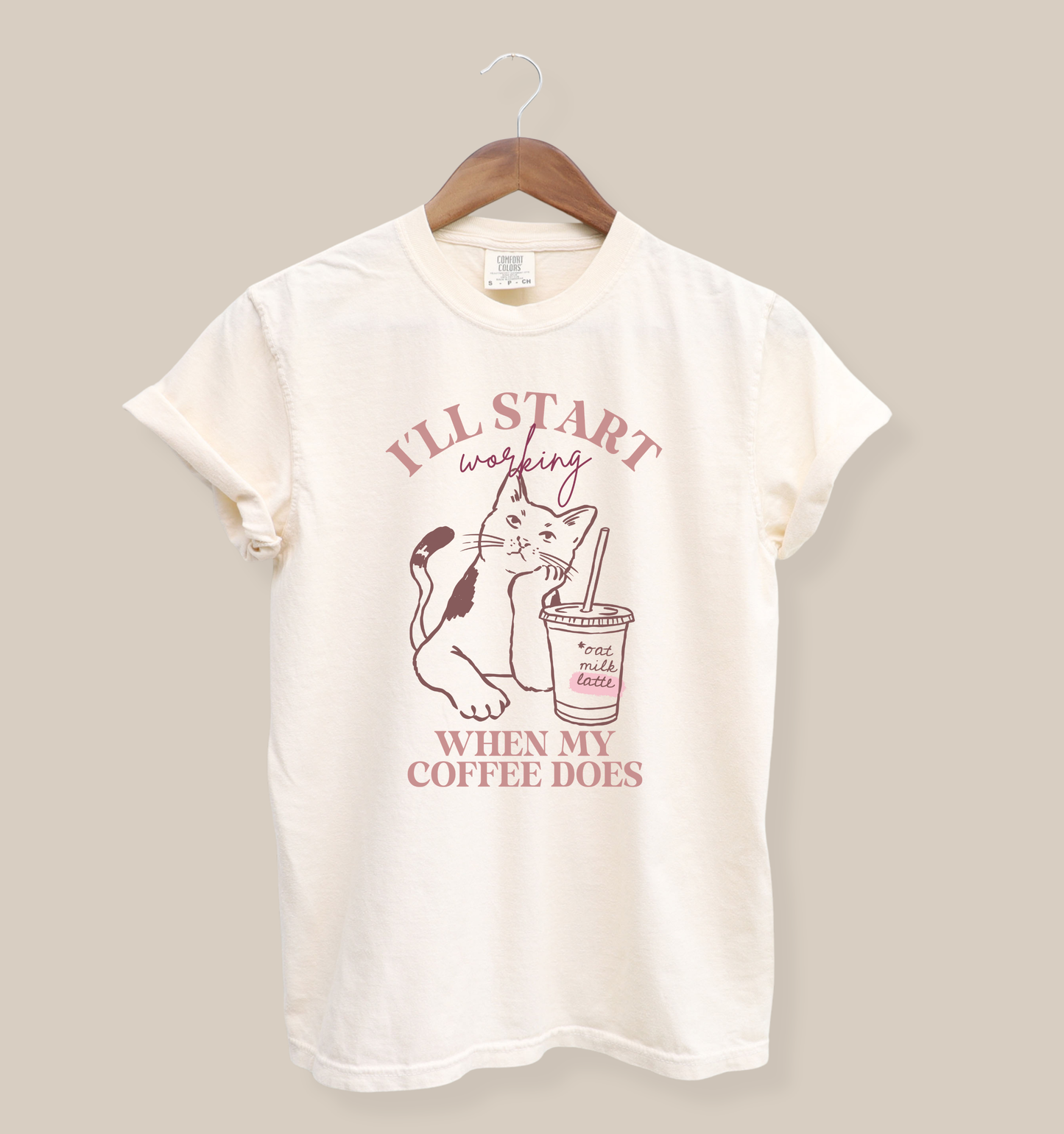 Comfort Colors 1717 garment-dyed t-shirt in ivory featuring an “I’ll Start Working When My Coffee Does” graphic with a cat and iced oat milk latte illustration.