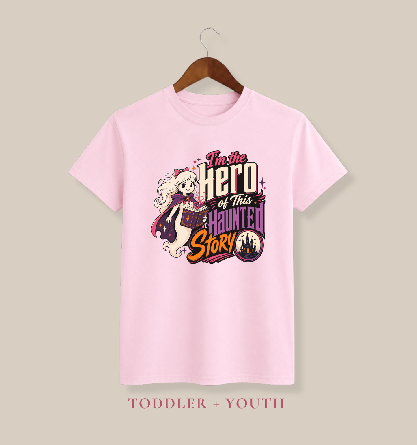 Pink youth T-shirt featuring a caped ghost with a magical book, sparkling stars, a haunted castle, and an empowering Halloween phrase.