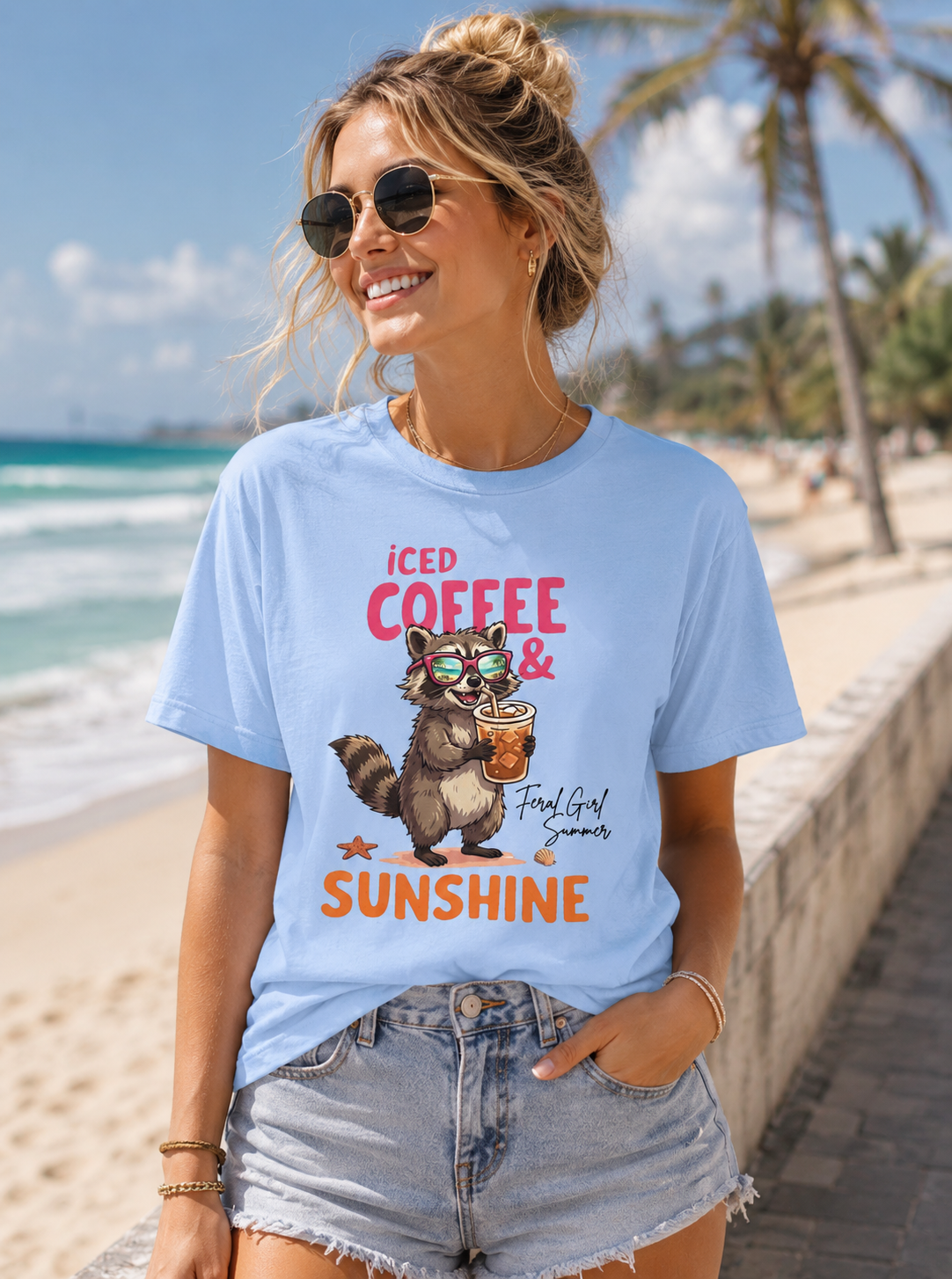 Woman wearing a Bella + Canvas 3001 t-shirt in baby blue featuring a raccoon wearing sunglasses and holding an iced coffee with the phrase “Iced Coffee & Sunshine” in colorful summer-inspired lettering.