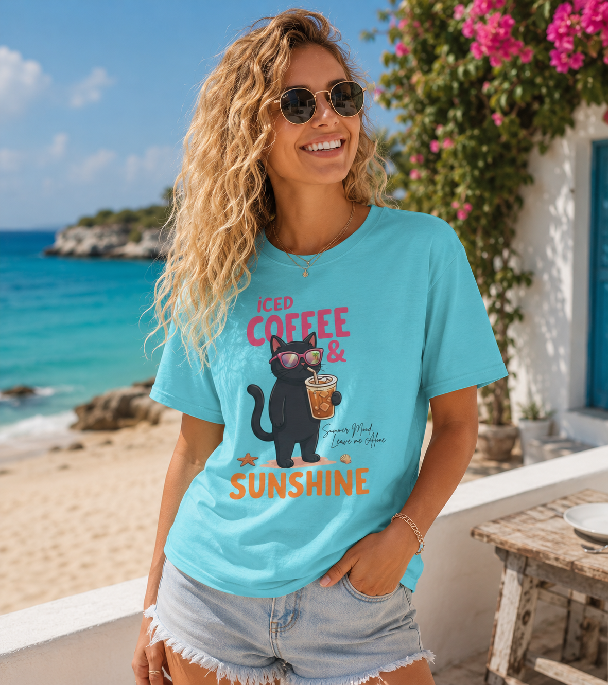 Woman wearing a Bella + Canvas 3001 t-shirt in turquoise featuring a black cat with sunglasses holding an iced coffee and the phrase “Iced Coffee & Sunshine” in a colorful summer beach setting.