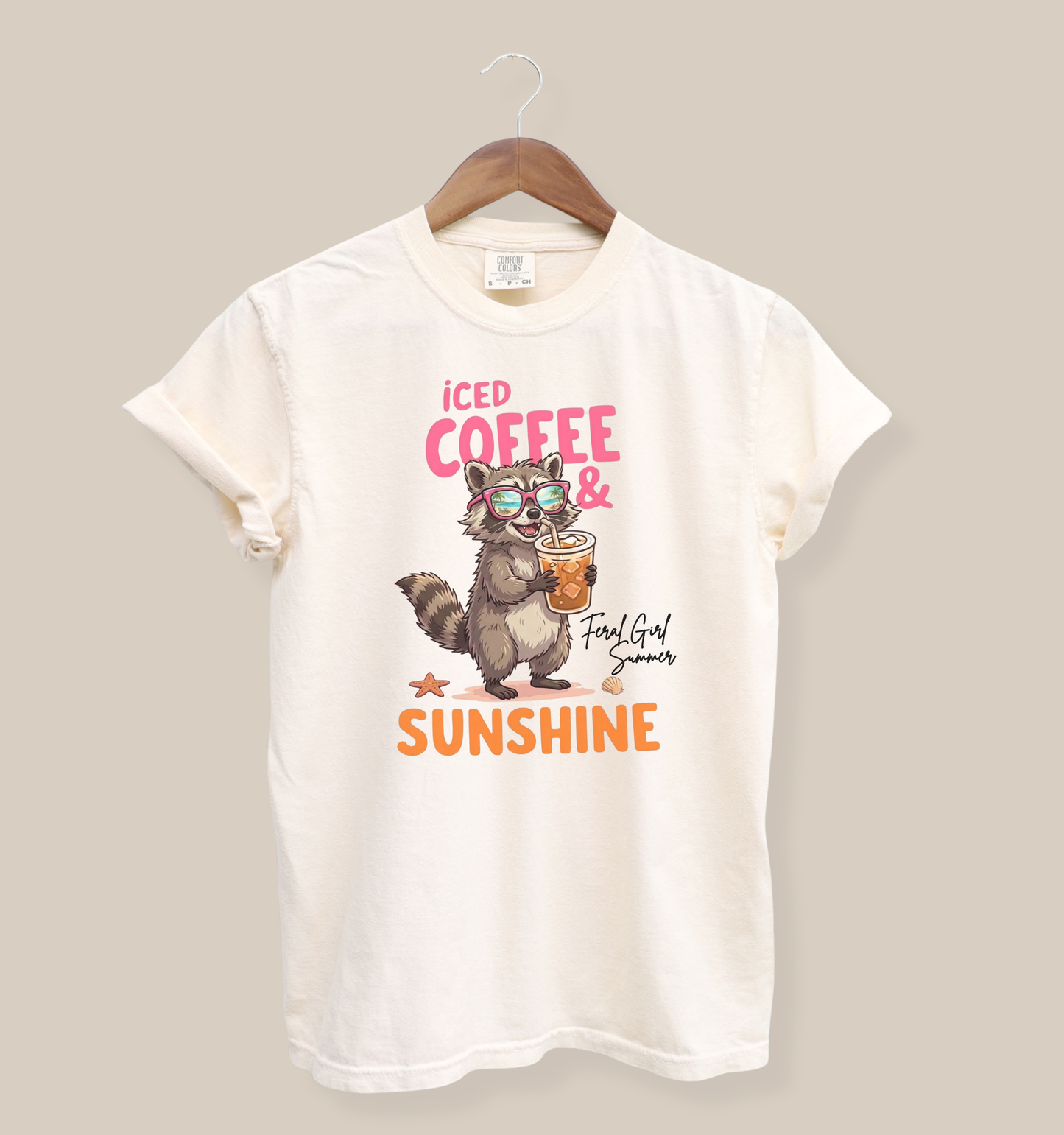 Comfort Colors 1717 t-shirt in ivory featuring a raccoon wearing sunglasses and holding an iced coffee with the phrase “Iced Coffee & Sunshine” in bright summer-inspired lettering.