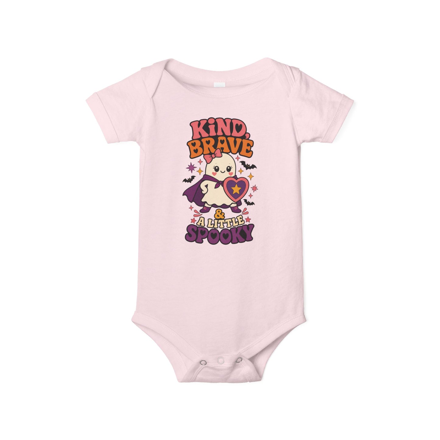 Pink baby one piece featuring a caped ghost holding a heart shield, colorful stars, bats, and the phrase “Kind, Brave & a Little Spooky.”