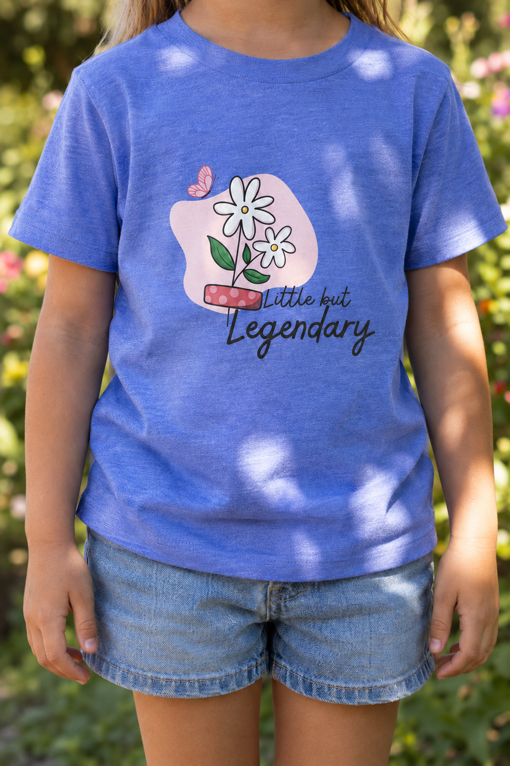 Child wearing a heather Columbia blue toddler T-shirt featuring daisies, a pink bandage, a butterfly, and the phrase “Little but Legendary.”