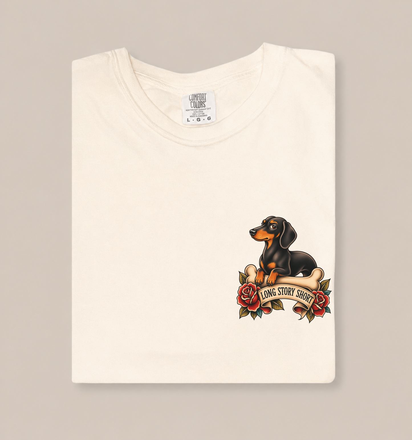 Ivory garment-dyed adult T-shirt featuring a tattoo-style dachshund resting on a bone above red roses and a humorous banner.