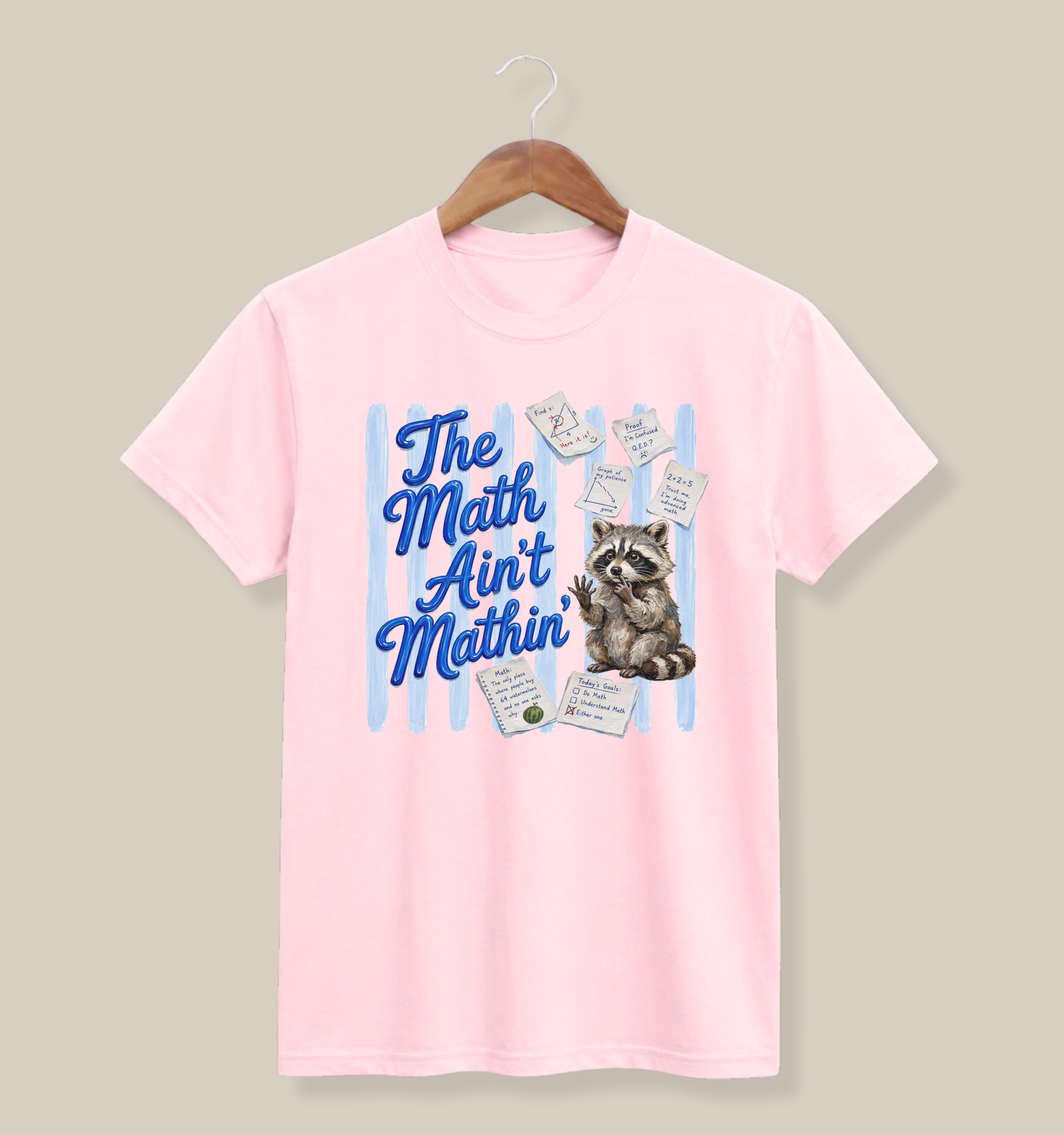 Bella + Canvas 3001 t-shirt in soft pink featuring the phrase “The Math Ain’t Mathin’” in blue script with a confused raccoon surrounded by math notes, equations, and classroom papers. Funny math teacher shirt for educators, algebra teachers, middle school teachers, high school math teachers, tutors, and STEM educators who appreciate classroom humor.