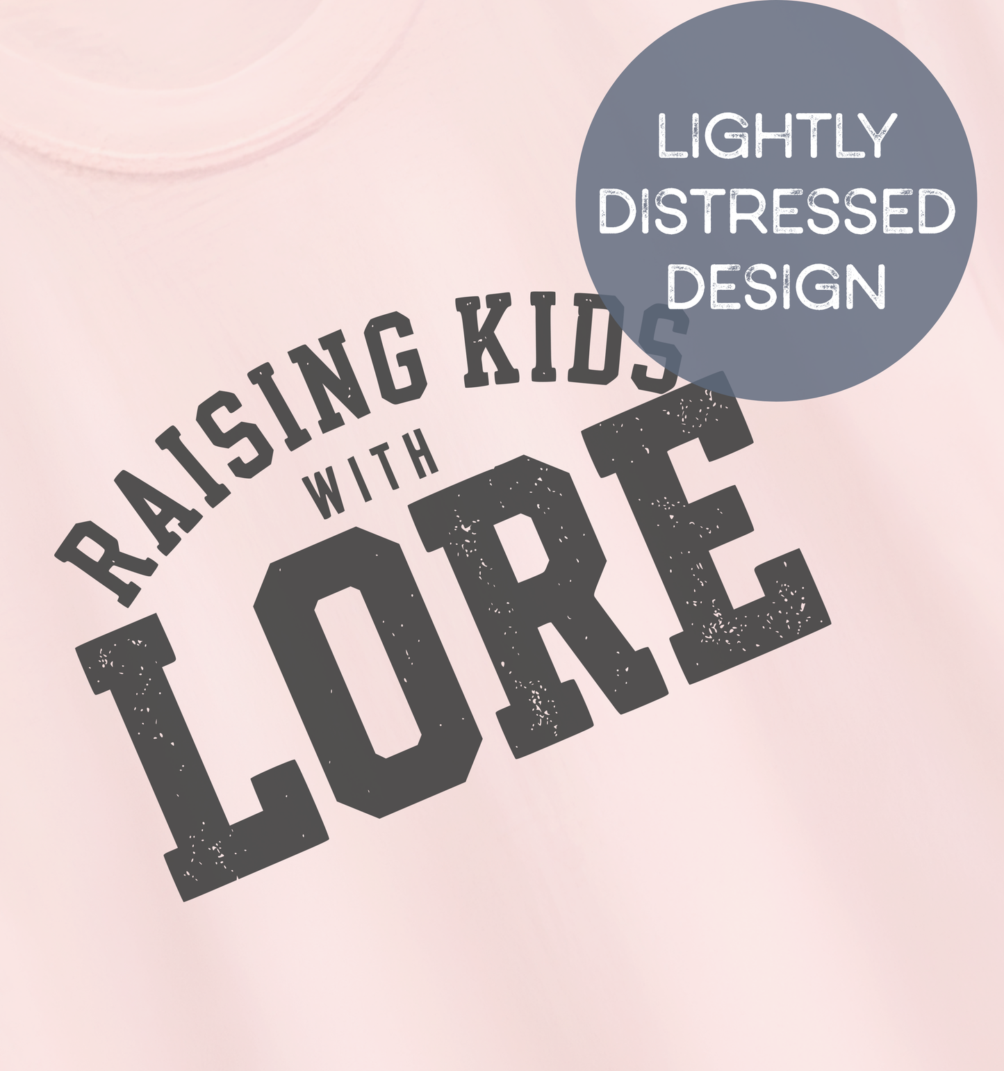 Close-up of a soft pink adult T-shirt featuring lightly distressed charcoal varsity lettering and the humorous phrase “Raising Kids With Lore.”