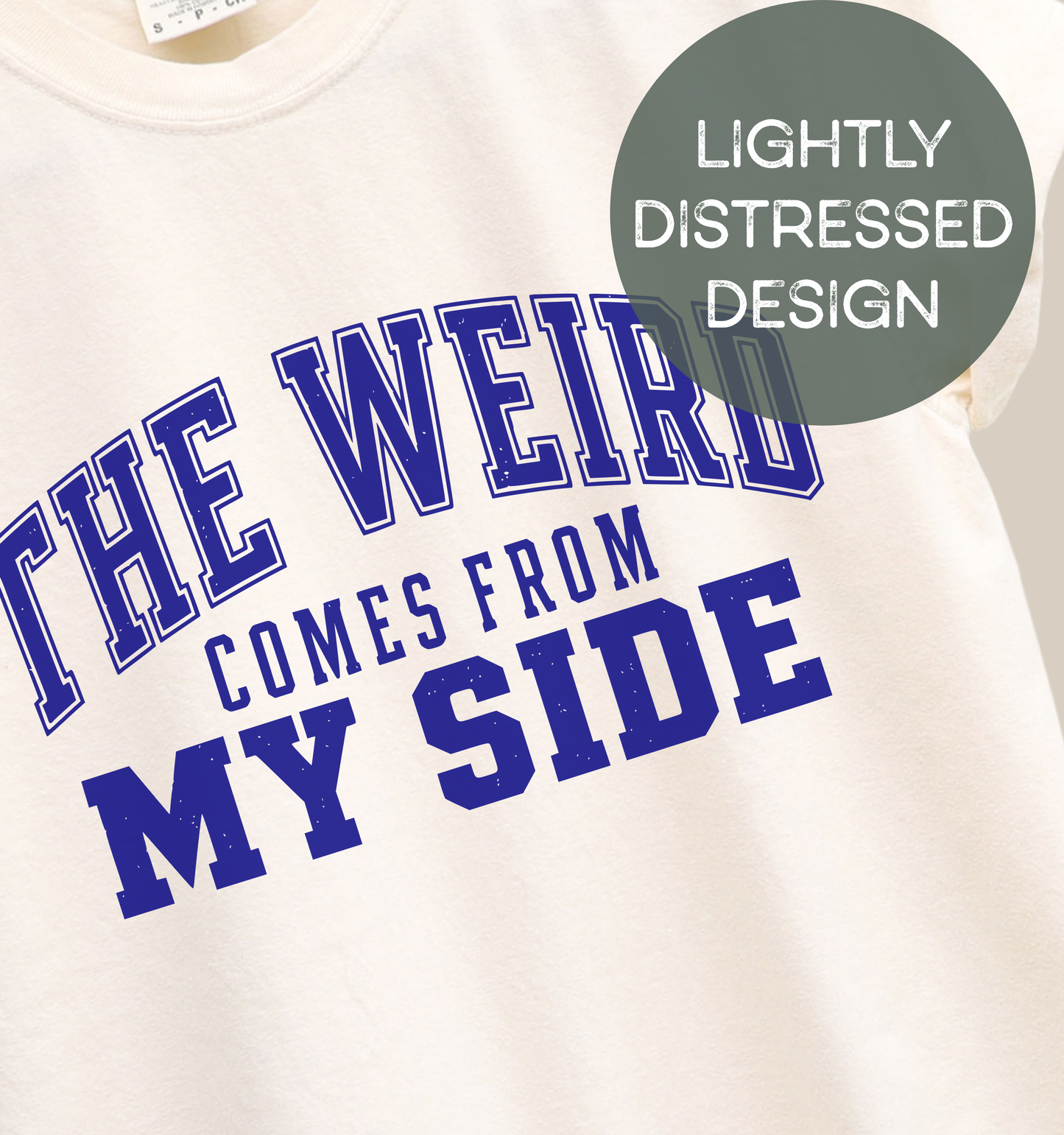 Close-up of a natural adult T-shirt featuring a lightly distressed blue varsity-style design with the humorous phrase “The Weird Comes From My Side.”