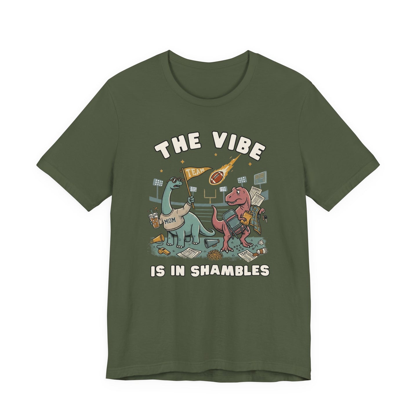 Bella + Canvas 3001 military green t-shirt featuring two stressed dinosaurs at a football stadium with a folding chair, coffee, snacks, team flag, and game day gear. Funny sports mom graphic tee with "The Vibe Is In Shambles" design, perfect for football moms, sports parents, weekend tournaments, tailgates, and busy game day schedules.