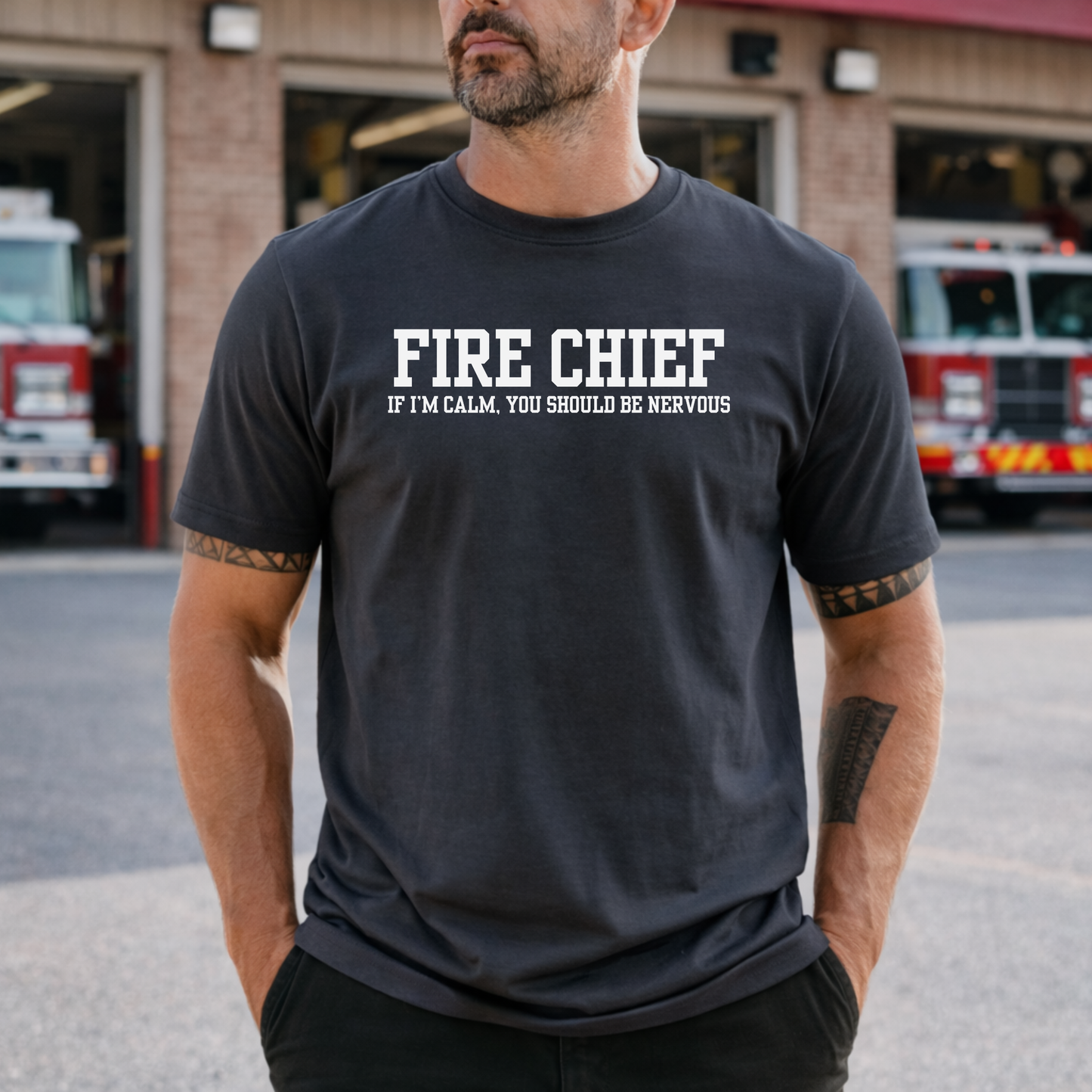 firefighter themed graphic t-shirt worn by man in front of fire station with fire trucks in background