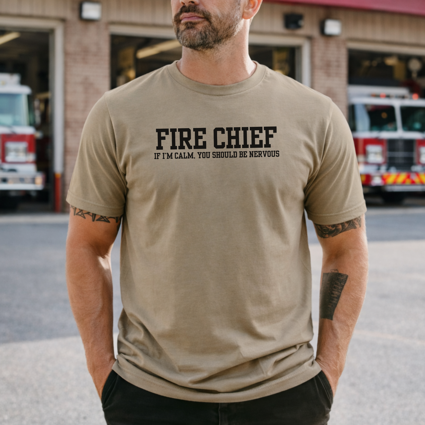 man wearing tan t-shirt with “Fire Chief If I’m Calm You Should Be Nervous” text standing in front of fire station