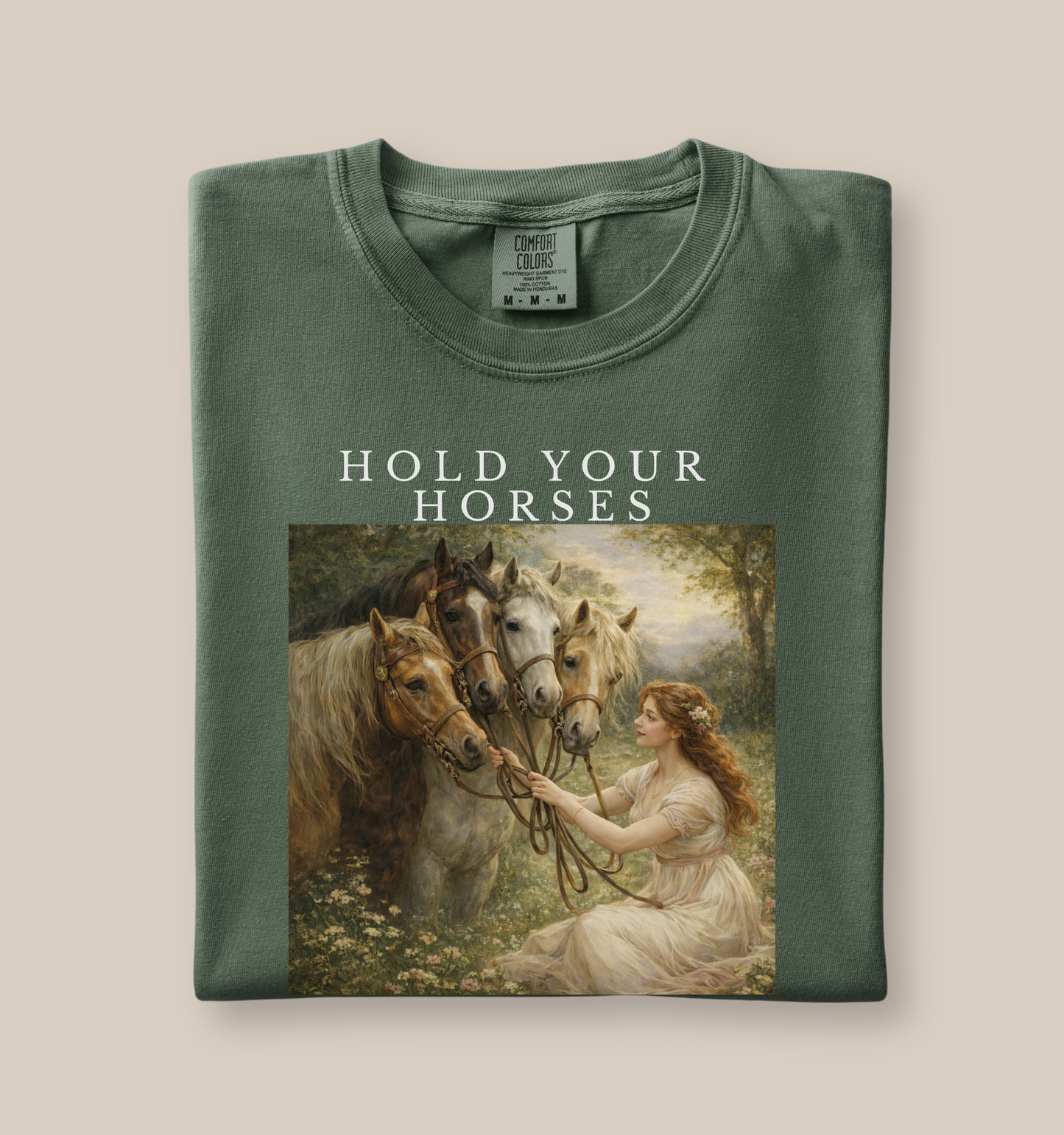 green t-shirt with “Hold Your Horses” text and vintage style artwork of woman with multiple horses, folded flat lay